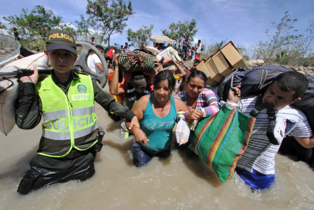Colombian police help Colombian women carry their belongings as they cross the Tachira border river from Venezuela to Colombia