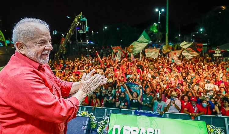 Lula is seen smiling on stage with supporters on the background