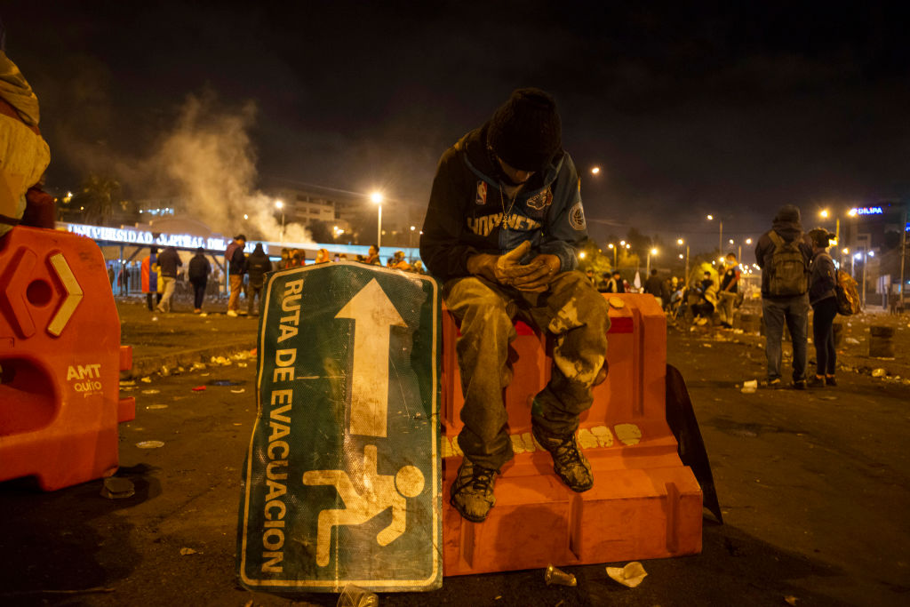 A protester in Ecuador rests next to a street sign showing an escape route.