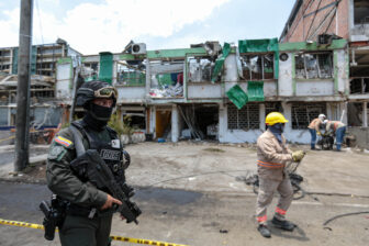 A member of the Colombian National Police's Special Operations Group stands guard as cleaners clear debris from the site of a bomb explosion in Cali, Colombia in August.