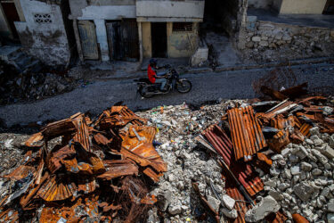 A motorcyclist drives by houses destroyed by armed gangs in 2024 in Port-au-Prince, Haiti in March 2026